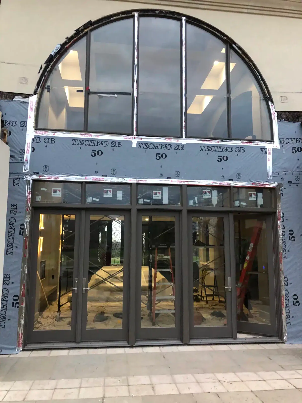 New black-framed glass entry doors with a half-round transom window during installation