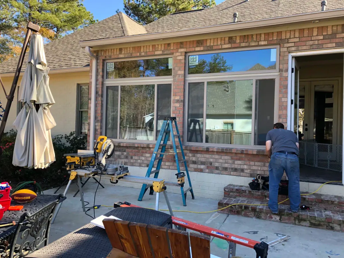 Installer working on new windows for a brick home addition with tools set up on the patio