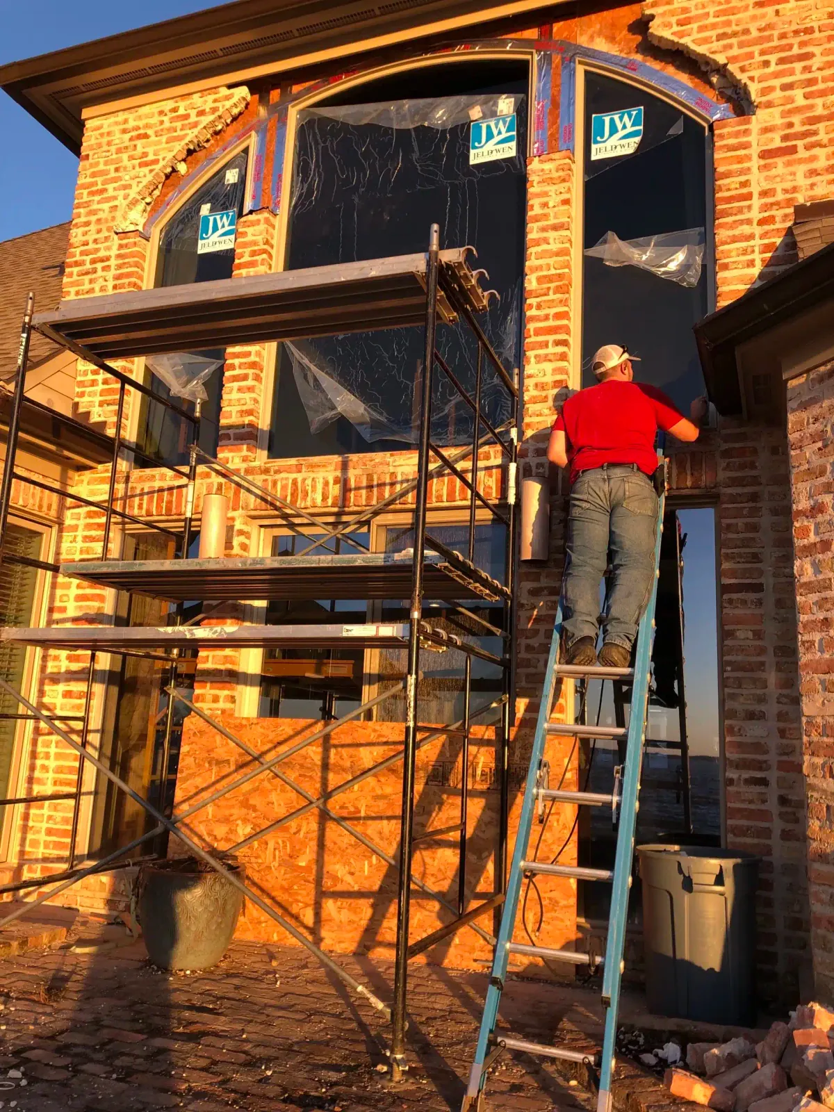 Installer on a ladder fitting a new arched window into a brick home at sunset