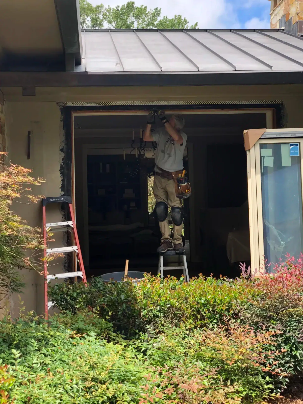 Installer on a ladder replacing a window on a home with a standing-seam metal roof