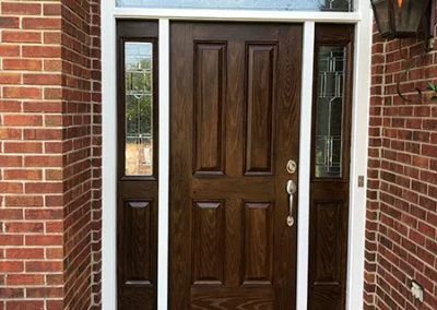 Dark stained wood entry door with leaded-glass sidelights on a brick home
