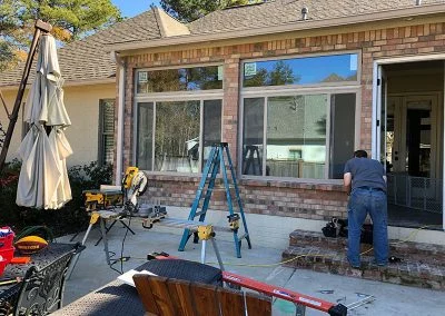Installer working on new sunroom windows from a brick patio